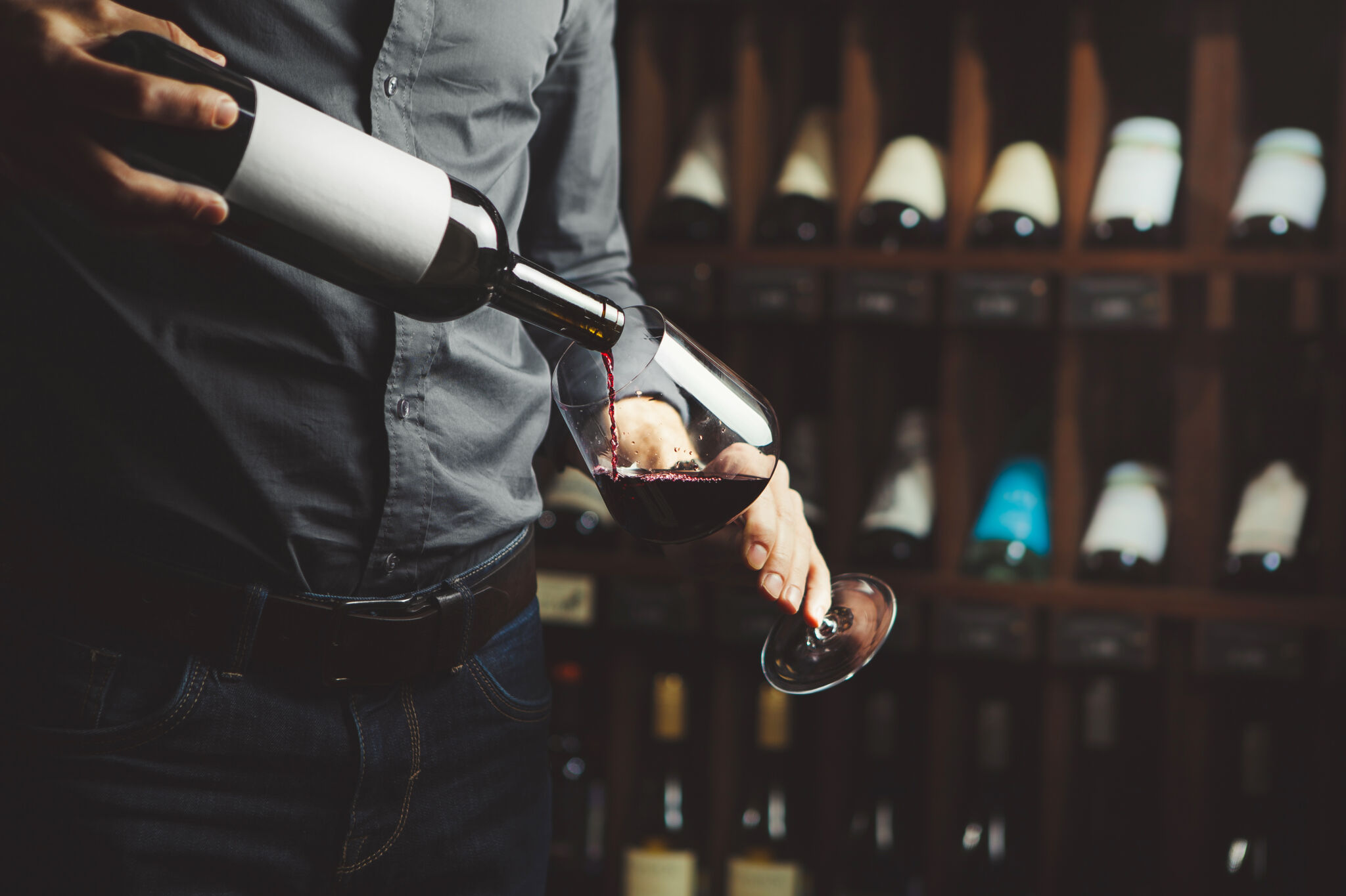 Close up shot of sommelier pouring red wine from bottle in glass on underground cellar background